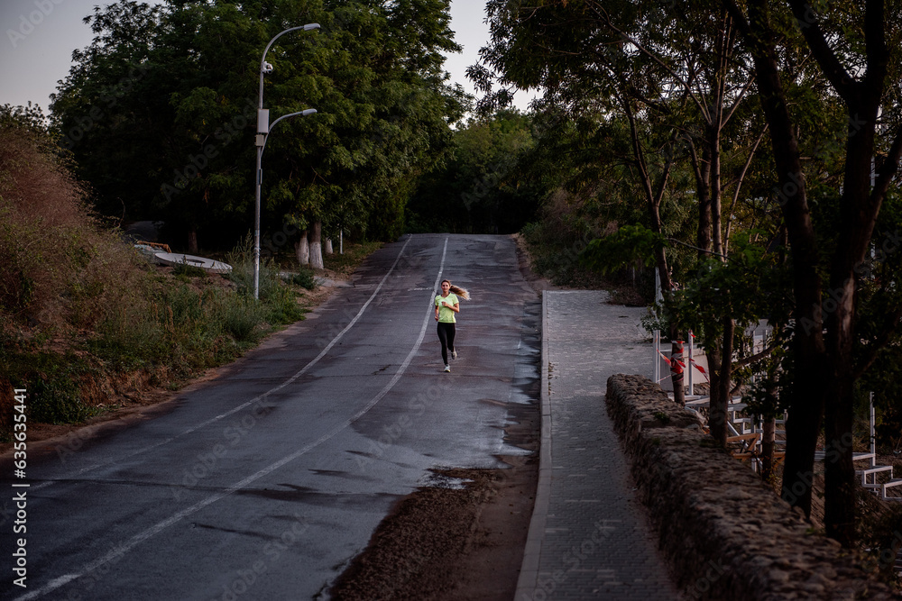 Obraz premium Young woman in sportswear is jogging early in morning on green track at sunrise. Pursuit of goals