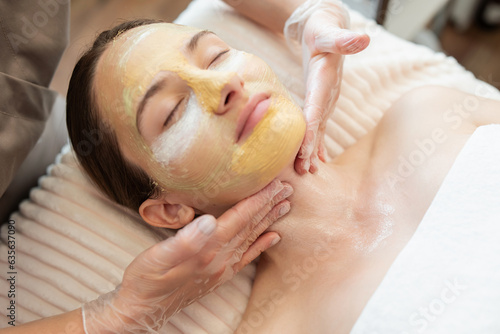 Tableau sur toile Young girl enjoying spa procedures with moisturizing, cleansing, brightening masks, while cosmetology specialist applying them to her face and neck