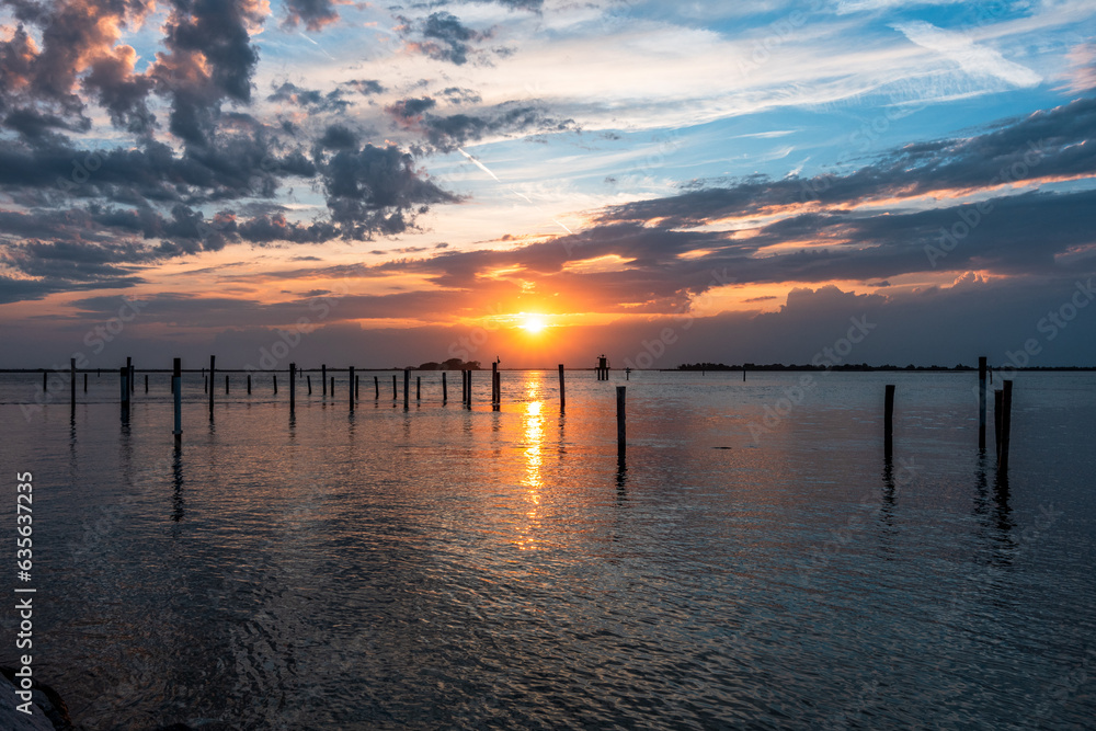 Sunset on the Grado Lagoon during a summer day. The sun is about to disappear over the horizon. Orange color and warm tones that make the atmosphere magical. Taken near the port.