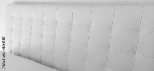 Soft headboard. Upholstery for furniture made of genuine or artificial leather and quilted fabric. Soft headboard against a light wall. Black and white monochrome photo