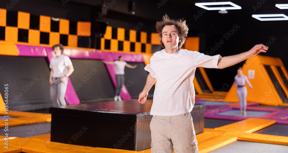 Young sports guy training to do jumps in trampoline center