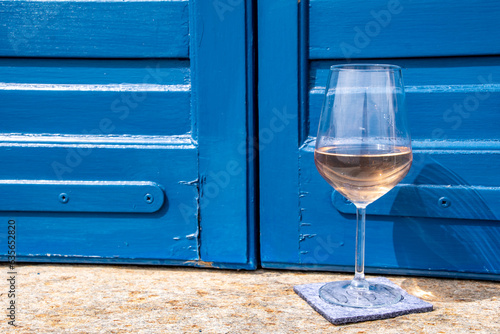 Glass of rose colored white wine on a balcony overlooking the Aegean Sea, blue shutters, and traditional village church spire - blue, refreshing, mood taken in Tinos Island, Greece