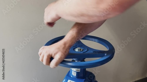 A man turning a large blue water supply valve (selective focus)