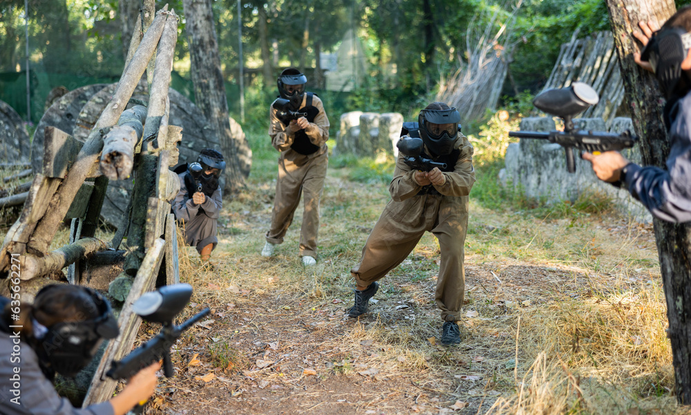 Fototapeta premium Group of friends paintball players of opposite teams in shootout in forest outdoors
