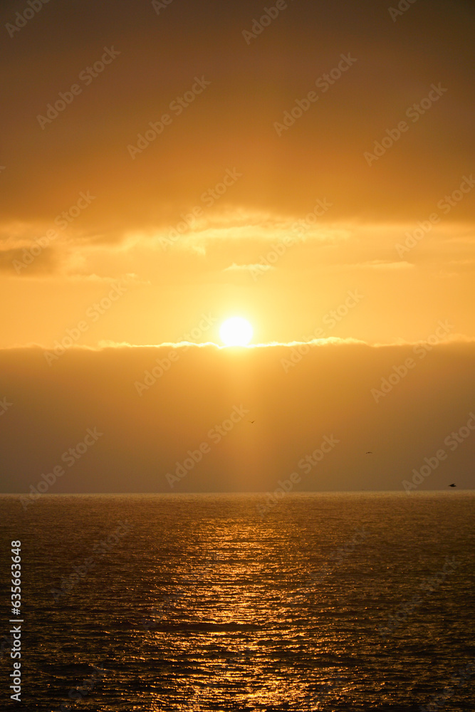 Vertical shot capturing the serene beauty of a golden orange sunset over the sea in Viña del Mar, creating a captivating and tranquil ambiance. Vertical shot capturing the serene beauty of a golden orange sunset over the sea in Viña del Mar, creating a captivating and tranquil ambiance.