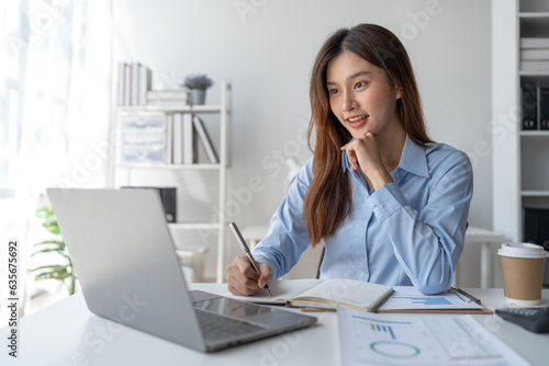 Confident asian businesswoman sitting and taking notes in notebook from laptop computer on financial, tax, income, expense, corporate issues for meeting preparation discuss in the office.