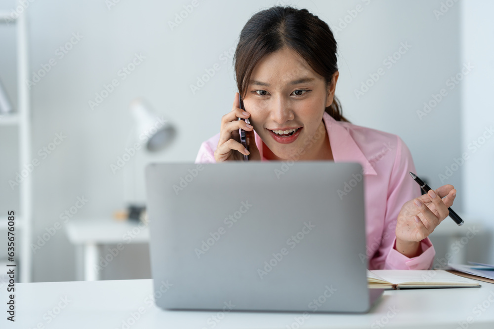 Happy young asian woman talking on the mobile phone and smiling while sitting at her working place in office. Happy young asian woman talking on the mobile phone and smiling while sitting at her working place in office.