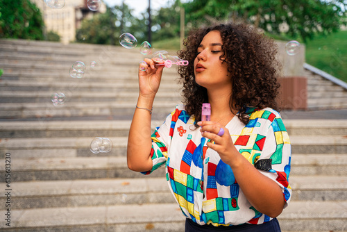 Young stylish female portrait, blowing bubbles outdoors