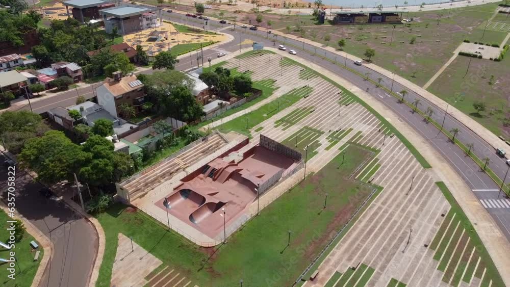 Drone wide flyover of skatepark and surrounding buildings and road with passing traffic - midday Drone wide flyover of skatepark and surrounding buildings and road with passing traffic - midday