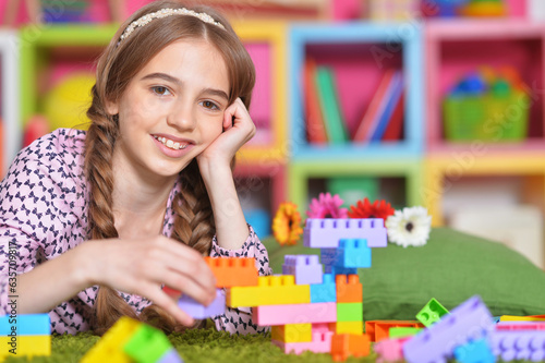 Portrait of cute girl playing with colorful plastic blocks in room