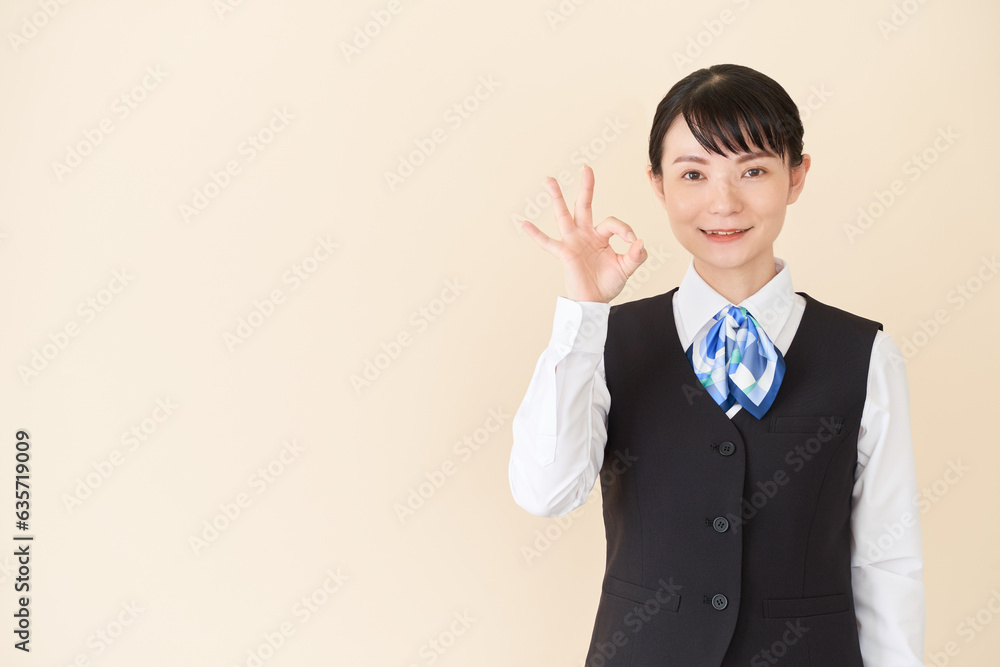 OKサインを出すベストにリボンタイの制服を着た、受付業務、事務業務の女性