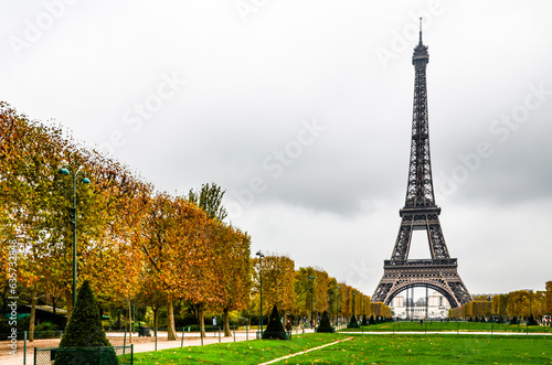 Autumn's golden embrace guides the eye along a scenic path, unveiling the iconic Eiffel Tower standing tall in the heart of Paris