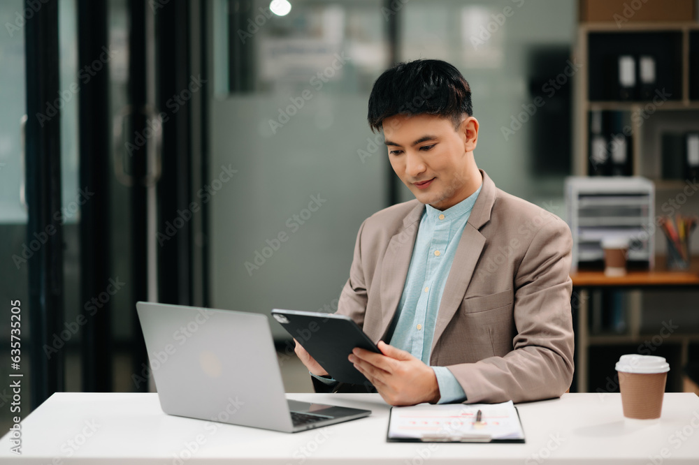 Young Asian business man working at office with laptop, tablet and taking notes on the paper. Young Asian business man working at office with laptop, tablet and taking notes on the paper.