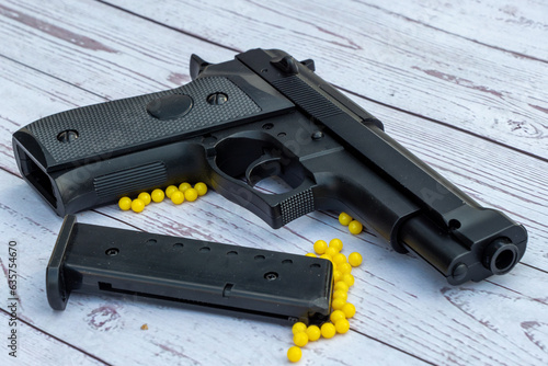airsoft handgun with yellow bb, on white wooden background
