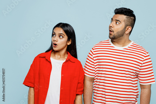 Young shocked surprised astonished couple two friends family Indian man woman wearing red casual clothes t-shirts look aside on area together isolated on pastel plain light blue cyan color background. photo