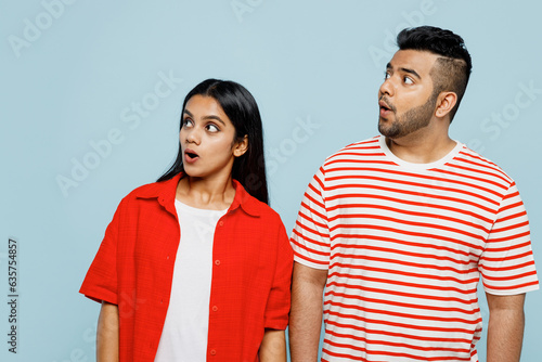 Obraz na plátně Young shocked surprised astonished couple two friends family Indian man woman wearing red casual clothes t-shirts look aside on area together isolated on pastel plain light blue cyan color background