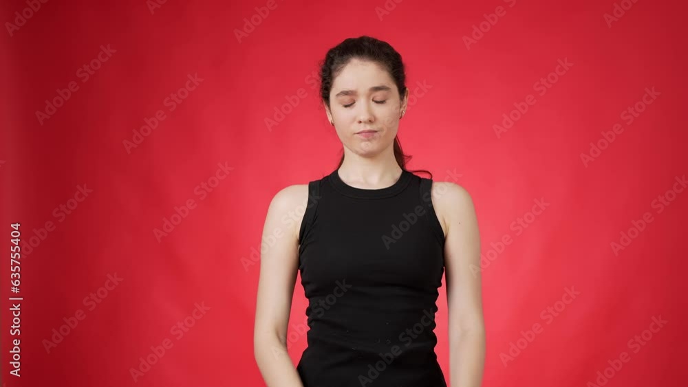 Young ponytailed dark haired woman dressed in black sleeveless top crossing her arms in forbidden sign and shaking her head sideways against red background Young ponytailed dark haired woman dressed in black sleeveless top crossing her arms in forbidden sign and shaking her head sideways against red background