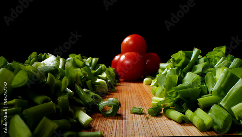 Cutting, cooking process, tasty and bright image, green onion with a bright tomato, on a dark background.
