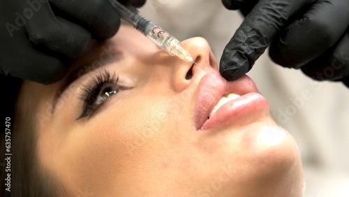 A beautician in medical gloves carefully and slowly injects hyaluronic acid into the lips of a young woman with a syringe. lip augmentation procedure. beauty injections. photo
