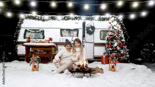 Принти на полотні A guy and a girl near a Christmas tree with garlands and a camper