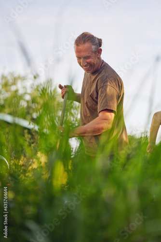 Male gardener raking the the flower bed while the collegue is sweeping the terrace in summer