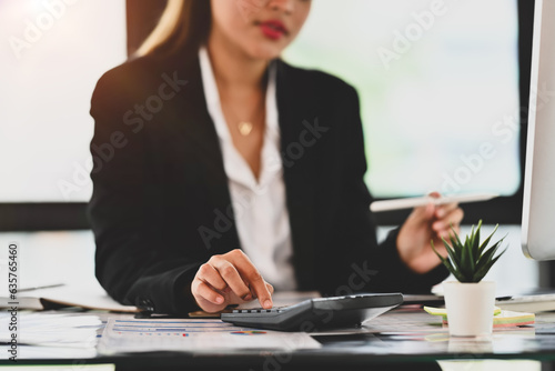 Cropped image of female economist analyzing sales statistics document, using calculator at her working desk