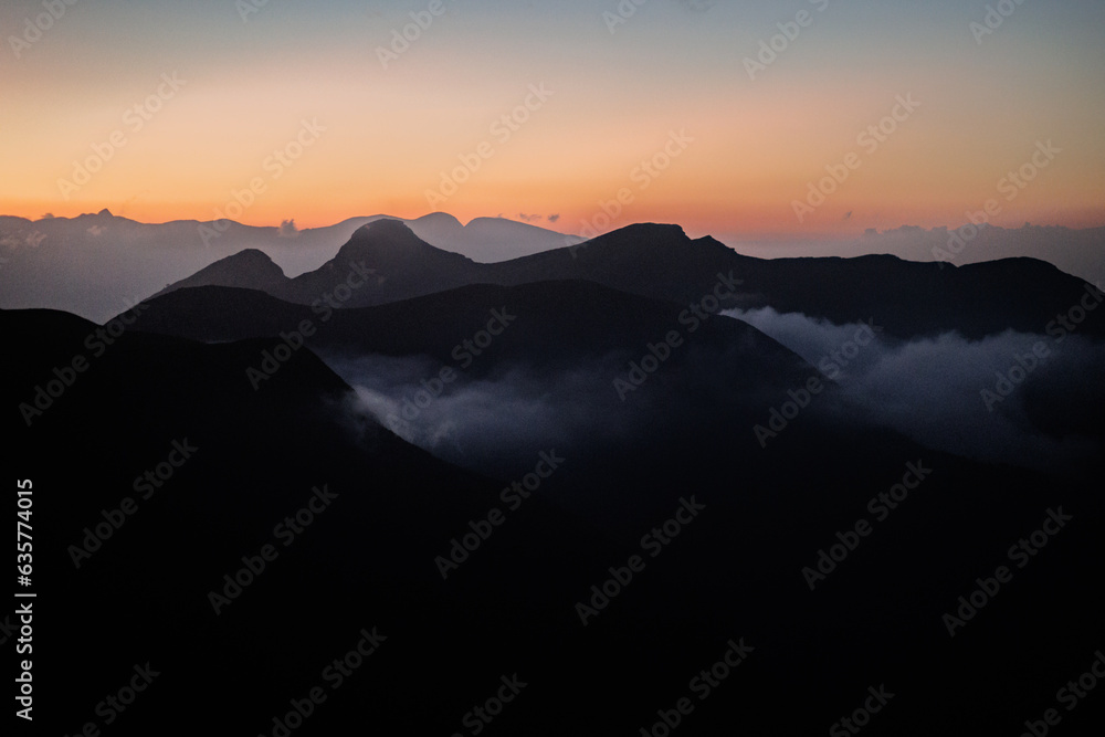 Obraz premium A flawless sunset paints the backdrop behind the silhouetted black mountains.