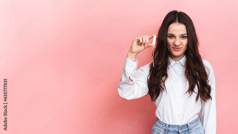 A young woman holds a menstrual swab in her hands. Pink background. Space for text. The concept of feminine hygiene. A young woman holds a menstrual swab in her hands. Pink background. Space for text. The concept of feminine hygiene.