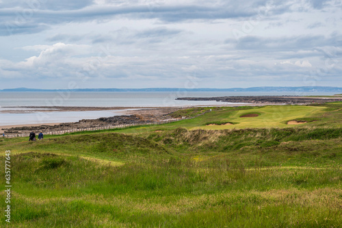 View of a fairway on a links golf course, overlooking the sea, in Wales. Bunkers can be seen, with the green in the distance. The day is cloudy. Room for copy photo