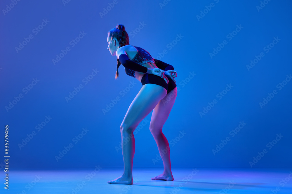 Young woman, professional volleyball player showing game combination with fingers against blue studio background in neon light. Concept of professional sport, competition, health, hobby, action, ad