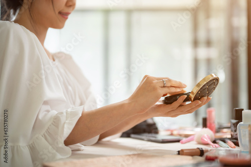 Close-up image of a beautiful Asian woman holding a compact powder or cushion