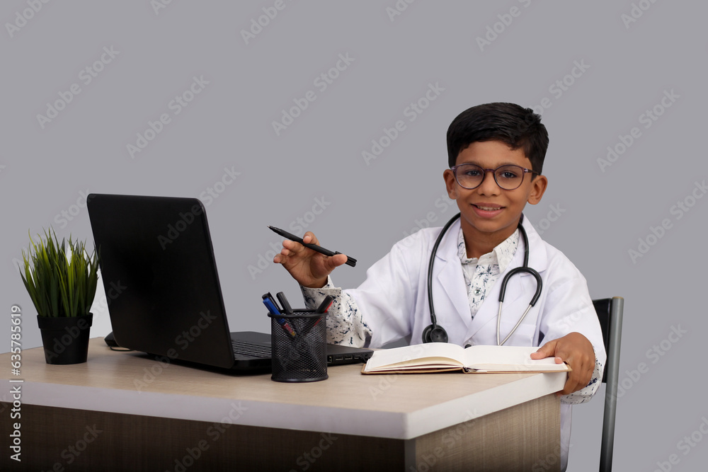 Indian Asian kid boy aged 7 to 8, wearing a doctor apron with stethoscope. with laptop writing prescription. He had a dream to future study as Doctor. He smiled happily, Concept little Doctor Indian Asian kid boy aged 7 to 8, wearing a doctor apron with stethoscope. with laptop writing prescription. He had a dream to future study as Doctor. He smiled happily, Concept little Doctor
