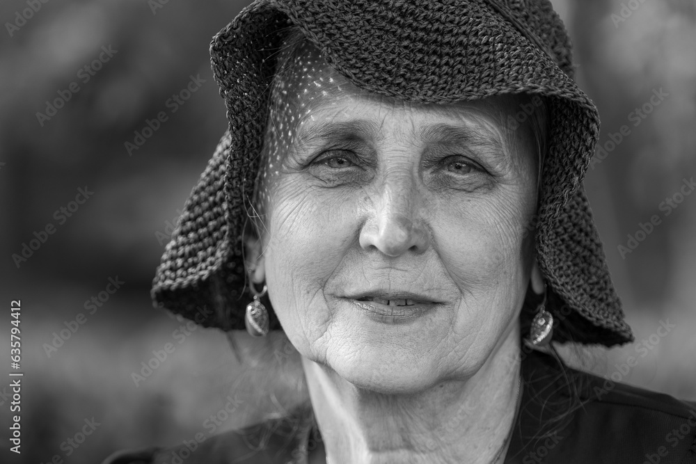 Portrait of a happy elderly woman 65 - 70 years old in a straw hat on the background of nature, closeup. Black and white Portrait of a happy elderly woman 65 - 70 years old in a straw hat on the background of nature, closeup. Black and white