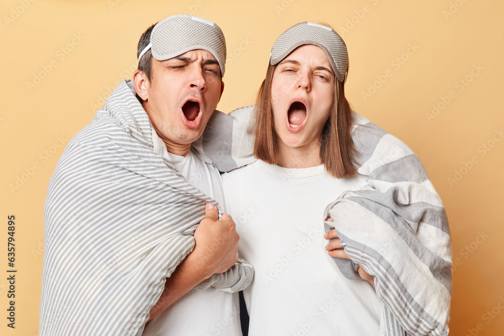 Sleepy couple man and woman wrapped in blanket isolated over beige background standing with closed eyes yawning with widely open mouth have not enough sleep. Sleepy couple man and woman wrapped in blanket isolated over beige background standing with closed eyes yawning with widely open mouth have not enough sleep.
