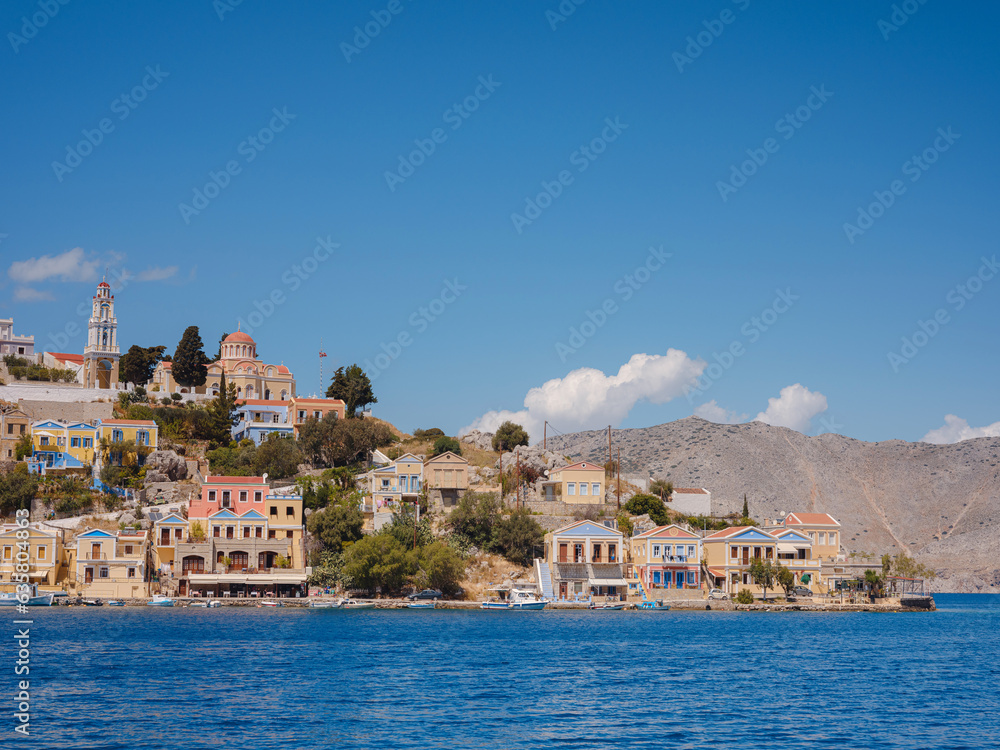 Naklejka premium Symi Island, Greece. Greece islands holidays from Rhodos in Aegean Sea. Colorful neoclassical houses in bay of Symi. Holiday travel background.