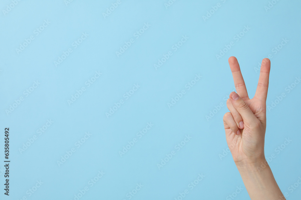 Female hand showing two fingers on a blue background, place for text Female hand showing two fingers on a blue background, place for text