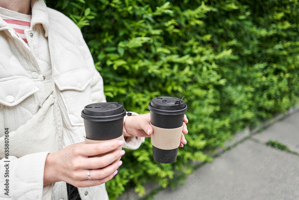 A girl in a residential neighborhood holds cups of coffee. Two glasses of hot drinks in the hands of a young woman. Breakfast on the go. Picnic and going out concept. A girl in a residential neighborhood holds cups of coffee. Two glasses of hot drinks in the hands of a young woman. Breakfast on the go. Picnic and going out concept.