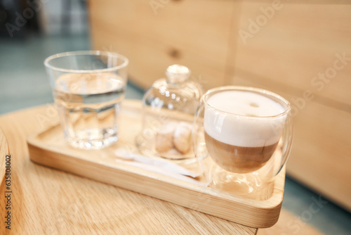 Cup of coffee cappuccino with cantuccini and a glass of water on a wooden tray. Coffee with milk, a cookie and a glass with water on a glass table. photo