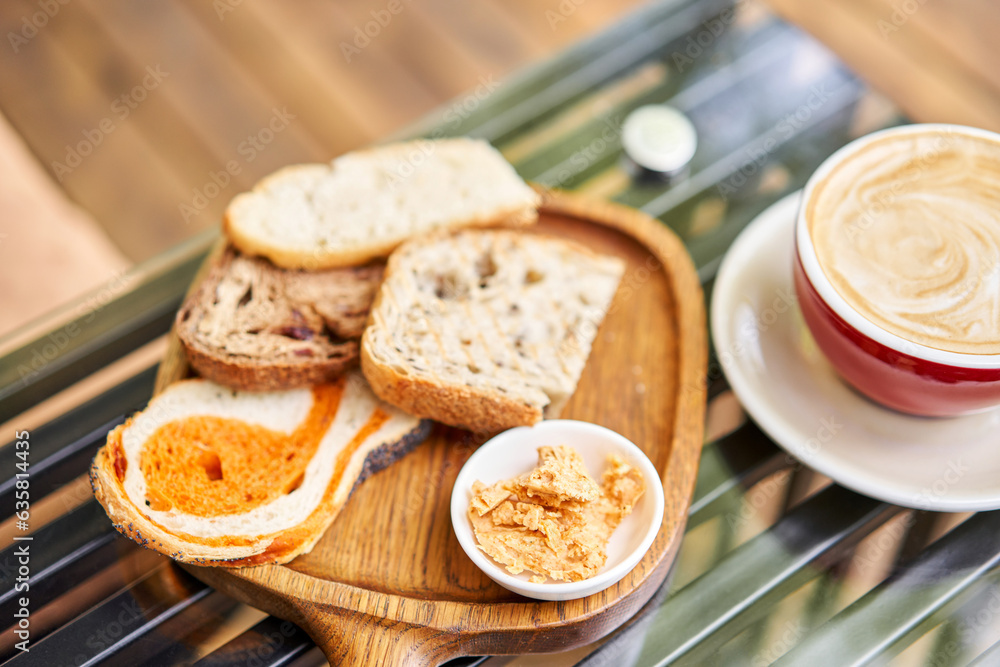 Assorted sliced bread on a wooden board. Served with smoked butter. Breakfast with cappuccino coffee. Composition with butter and bread on wooden plate. Assorted sliced bread on a wooden board. Served with smoked butter. Breakfast with cappuccino coffee. Composition with butter and bread on wooden plate.