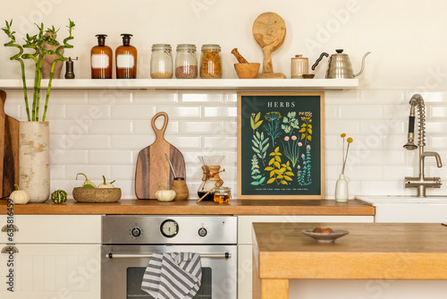 Creative composition of kitchen interior with mock up poster frame, silver oven, tap, stylish cup, jar with spices, brown bottle, white wall, tiles and personal accessories. Home decor. Template.