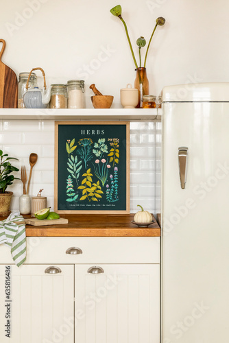 Interior design of kitchen space interior with mock up poster frame, fridge, jar with spices, pear, vase with flowers, kitchen board, plant in flowerpot and personal accessories. Home decor. Template.