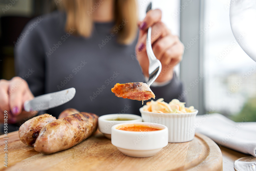 A piece of sausage is dipped in sauce. Lunch in a restaurant, a woman cuts Grilled sausages. Barbecue restaurant menu, a series of photos of different means. 