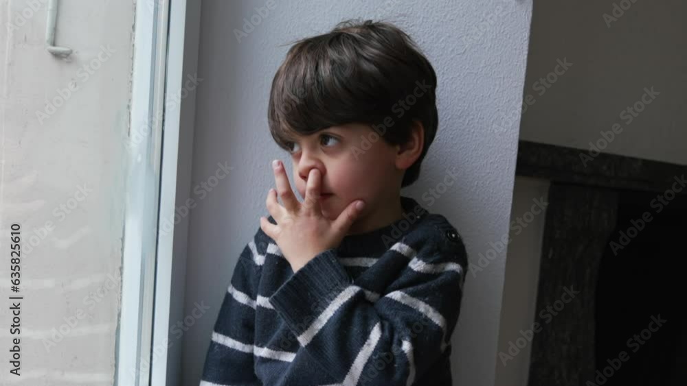 Child Nose Picking While Sitting by Window at Home Looking Out, Curious Kid in Thoughtful Observation