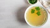 Chicken broth with parsley in bowl on white table. Copy space. Top view. Space for text.