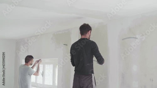 Construction workers plastering ceiling using hand tool and mortal on drywall and preparing surface for painting in house construction site. Men at work, caucasian young adults construction teamwork.  photo