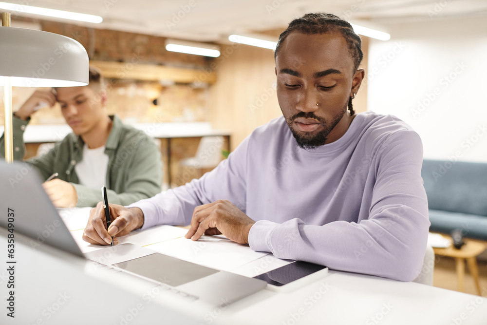 Fototapeta premium coworking, african american man taking notes, writing down ideas near gadgets, startup planning