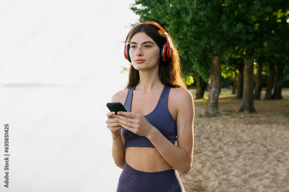 A young woman chooses music on her phone before jogging on the beach. The athlete trains outside. A young woman chooses music on her phone before jogging on the beach. The athlete trains outside.