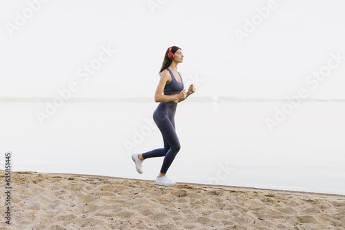 An athletic woman runs along the sea. Model in a tracksuit and headphones.