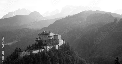 Rainy day panorama in austrian alps. Castle “Hohenwerfen“ in Werfen with silhouettes of mountain ranges in misty background. Black and white scenery with mystic atmosphere. photo