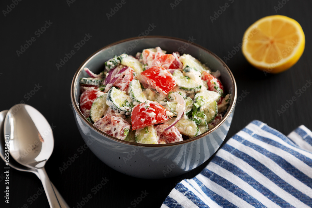 Homemade Tomato Cucumber Feta Salad in a Bowl on a black background, side view.